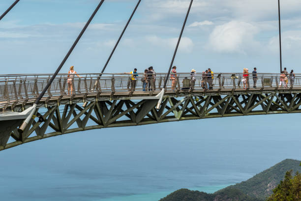les touristes visitent le pont de ciel sur la montagne dans le fond de la mer et l’île de langkawi, malaisie - tropical rainforest elevated walkway pulau langkawi malaysia photos et images de collection