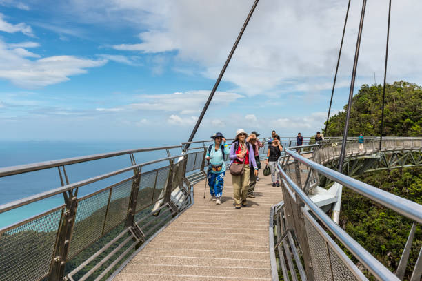 les touristes visitent le pont de ciel sur la montagne et les forêts tropicales dans l’île de langkawi de fond, malaisie - tropical rainforest elevated walkway pulau langkawi malaysia photos et images de collection