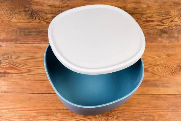 Empty plastic blue-gray salad bowl with slightly open gray lid on the rustic table, top view