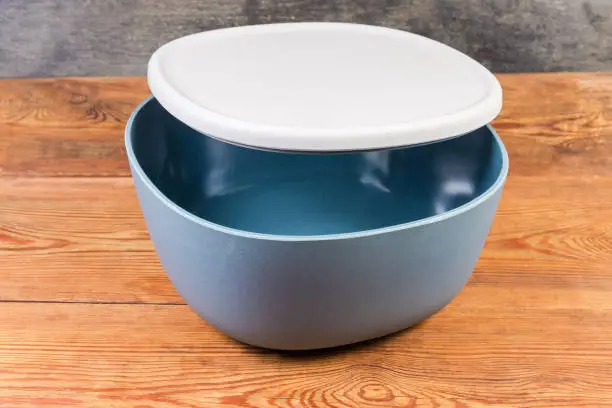 Empty plastic blue-gray salad bowl with slightly open gray lid on the rustic table