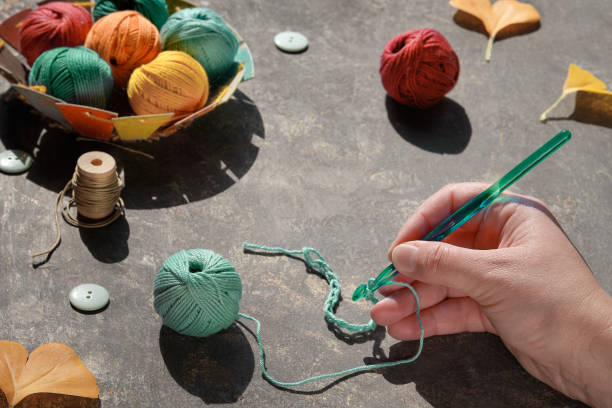 istock Hand with crochet hook with thread, yarn balls, buttons, felt pumpkins, Fall leaves. Autumn arrangement of craft materials for knitting and crochet on dark table. 1273825734