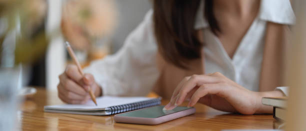 istock Female student searching information on mock up smartphone and write it down 1273826028