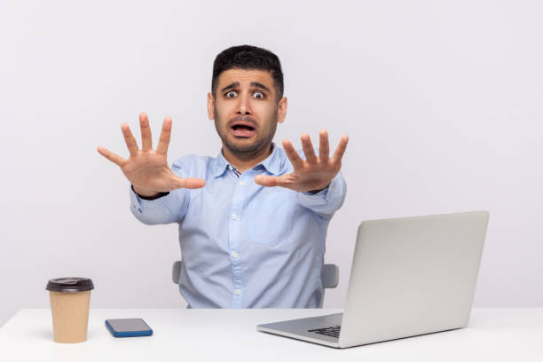 istock Scared man employee sitting office workplace with laptop on desk, raising hands stop gesture, looking desperate 1273827688