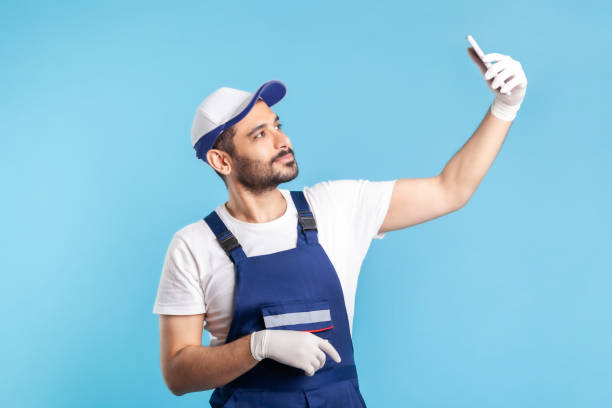 istock Workman in overalls and gloves talking on video call, communicating online with client using mobile phone 1273827813