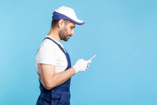 istock Side view, workman in overalls and gloves typing on mobile phone, using cellphone messenger to accept online order 1273827831