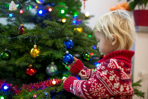 istock Cute little blonde boy with Christmas sweater, decorating christmas tree 1273830141