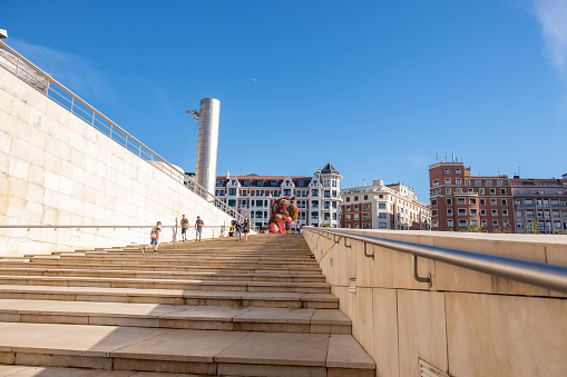 Bilbao, Biscay, Spain – September 08, 2020: Guggenheim Museum Bilbao. A small number of tourists and locals on the stairs next to the Guggenheim Museum in Bilbao