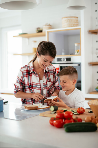 Mother making breakfast with son. Young family preparing delicious food in kitchen
