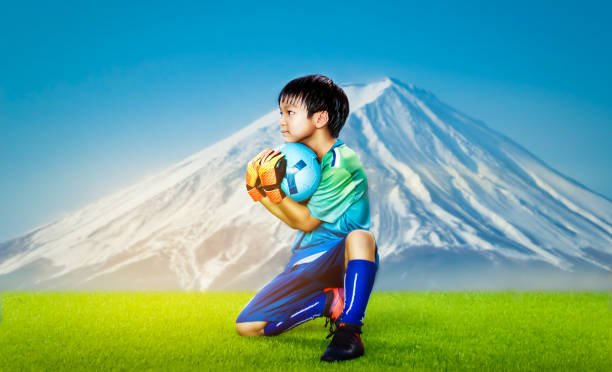 little kid torwart hält den ball auf einem rasenplatz mit fuji berg hintergrund für japanische jugendfußball. - playing field goalie soccer player little boys stock-fotos und bilder