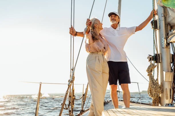 Elderly people standing on private sailboat and holding ropes