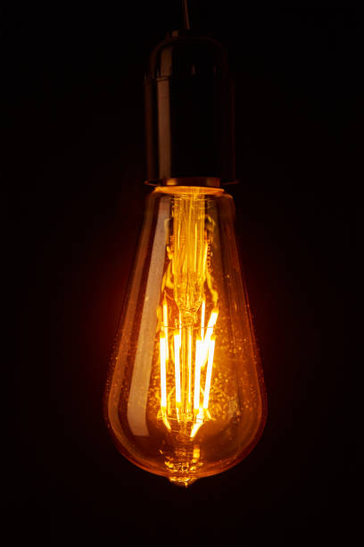 istock Vintage light bulb on black background, closeup. Glowing edison bulb 1273838093
