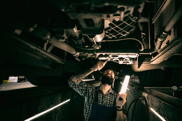 istock Car Mechanic working in car repair pit holding light 1273839434