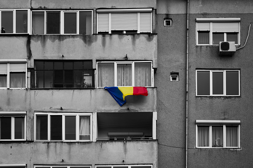 Oradea, Romania - December 10, 2017: A beautiful shot of the Romanian flag that is hanging from the balcony of a communist residential building edited with selective colors.