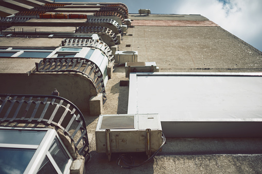 Oradea, Romania - May 28, 2018: A low angle view of an old communist apartment building with air conditioners, an empty ad billboard and balconies with cast iron railings.