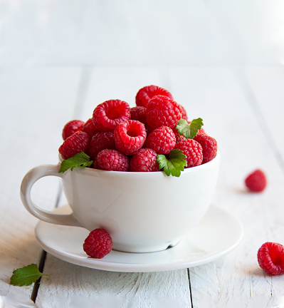 Ripe raspberries with leaves in white cup