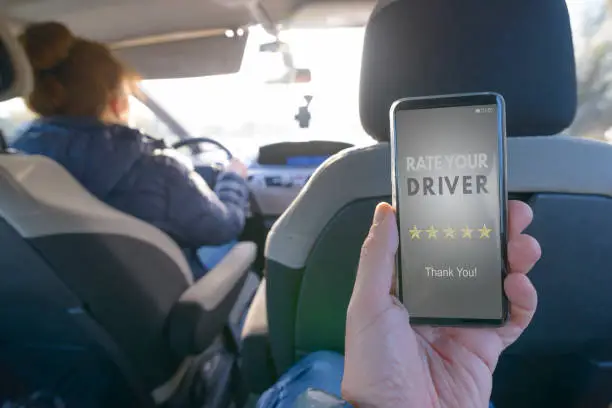 Passenger is sitting on the back seat of the car and using smart phone app to rate a driver. Taxi or modern peer to peer ridesharing concept