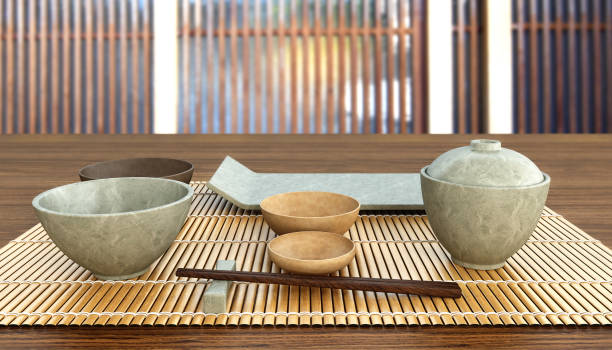 istock Japanese table setting. Concept image for traditional dining guide or oriental ceramics tableware set with main dish, side dishes, pickle, soup and chopsticks on bamboo mat. 3D rendering. 1273844498