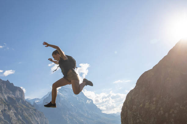 Young woman jumps off mountain ridge at sunrise North Face of the Eiger Mountain in distance, Swiss Alps eiger northface stock pictures, royalty-free photos & images