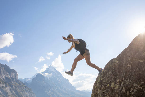 Young woman jumps off mountain ridge at sunrise North Face of the Eiger Mountain in distance, Swiss Alps leap of faith stock pictures, royalty-free photos & images