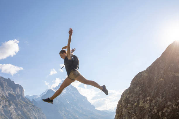 Young woman jumps off mountain ridge at sunrise North Face of the Eiger Mountain in distance, Swiss Alps leap of faith stock pictures, royalty-free photos & images