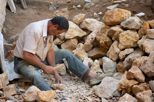 Beit Mery/Lebanon - 09/12/2020: a Lebanese stonemason is sitting in a pile of stone using his hammer to carve a stone