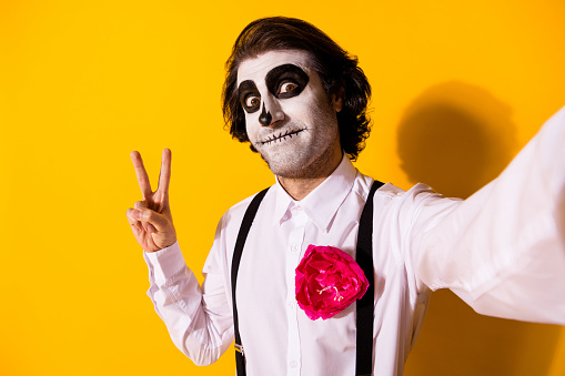 Self-portrait of nice handsome creepy scary baleful cheery malicious guy catrina, celebratory having fun showing v-sign social influencer isolated bright vivid shine vibrant yellow color background