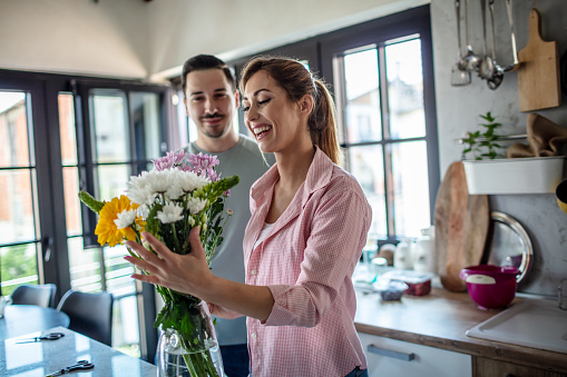 Young love couple arranging a flowers in vases at home.