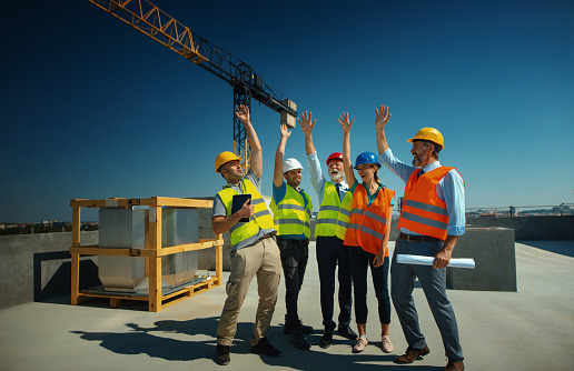 Closeup of group of building contractors and engineers on top of the building clasping hands while celebrating the end of construction.