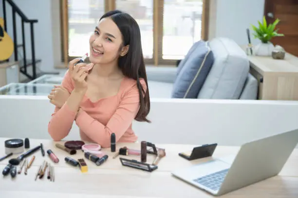 Photo of Portrait of young asian woman review giveaway gift product fan following channel, recording video make up lipstic cosmetic at home. Beauty blogger present beauty cosmetics