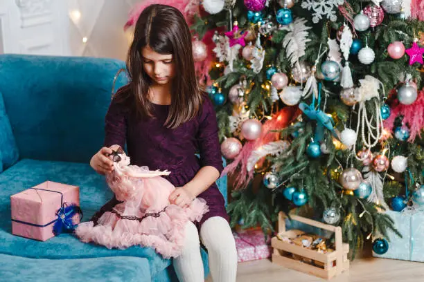 dark-haired seven-year-old girl plays with doll on new year's eve indoors