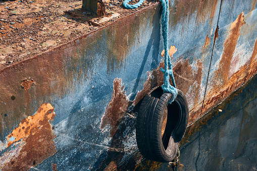 A close view of an abandoned rusty blue fishing boat that has a tire tied on its side.