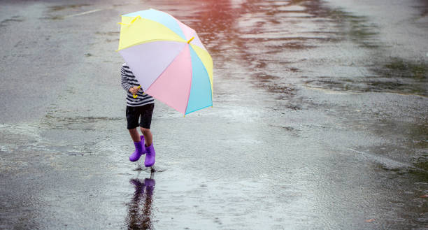 Little young human held a colorful umbrella playing in the rain happily on a rainy day. stock photo