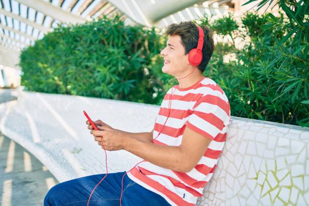 Young caucasian man smiling happy using touchpad and headphones sitting on the bench.