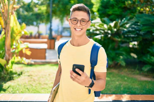 Young hispanic student smiling happy using smartphone walking the university campus