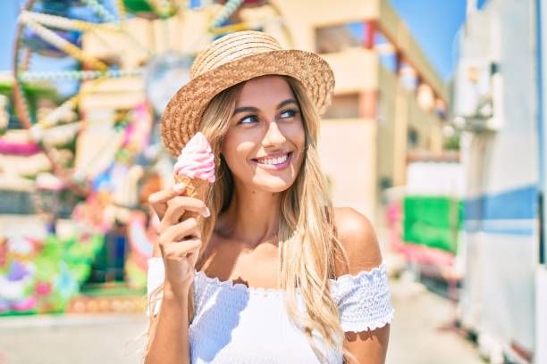 młoda blondynka turystka uśmiechnięta szczęśliwy jedzenia lodów na wesołym miasteczku. - people eating walking fun zdjęcia i obrazy z banku zdjęć