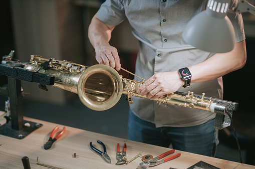 asian chinese male expertise repairing restoring alto saxophone at his work place