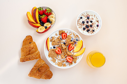 Summer breakfast. Granola and wheat flakes with fruits, berries and milk on a light pink background.