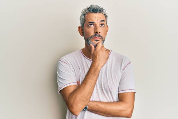 Middle age grey-haired man wearing casual clothes with hand on chin thinking about question, pensive expression. smiling with thoughtful face. doubt concept.