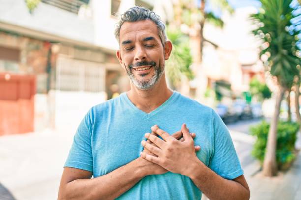 uomo dai capelli grigi di mezza età che indossa abiti casual in strada della città sorridendo con le mani sul petto con gli occhi chiusi e un gesto grato sul viso. concetto di salute. - fashion male beauty confidence elegance foto e immagini stock