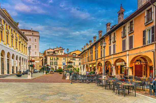 Typical italian buildings and tables of street restaurants on Piazza del Mercato Market square in Brescia city historical centre, evening twilight view, Italian street, Lombardy, Northern Italy