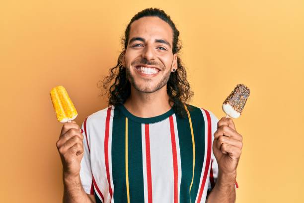 Young handsome man with long hair eating two ice cream smiling with a happy and cool smile on face. showing teeth. Young handsome man with long hair eating two ice cream smiling with a happy and cool smile on face. showing teeth. in pride we trust stock pictures, royalty-free photos & images