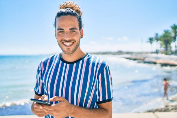 istock Young hispanic man smiling happy using smartphone at the beach. 1273861199