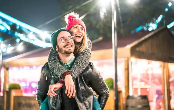 Photo of Happy couple in love enjoying winter travel time outdoor - Handsome guy with nice girl on piggy back moment - Relationship concept with boyfriend and girlfriend together on warm vivid neon filter