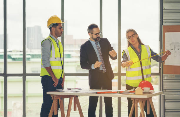 istock Team of multiethnic architects working on construction plans in meeting room. Engineers discussing on project in office. Mature businessman and woman standing around table working on blueprint. 1273868346