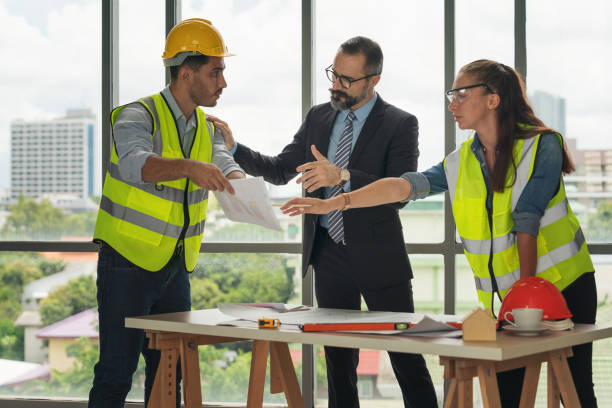 istock Team of multiethnic architects working on construction plans in meeting room. Engineers discussing on project in office. Mature businessman and woman standing around table working on blueprint. 1273868365