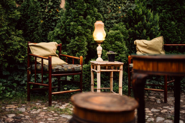 Cozy garden in the evening. Wooden rustic table, armchair and vintage lamp in lovely garden.