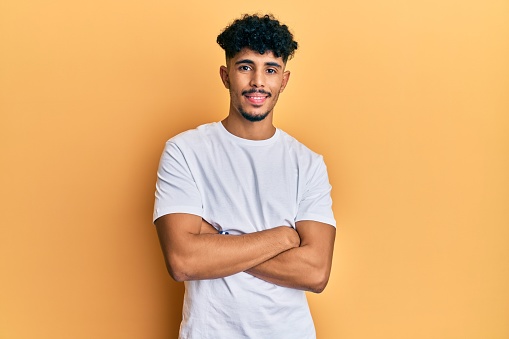 Young arab handsome man wearing casual white tshirt happy face smiling with crossed arms looking at the camera. positive person.