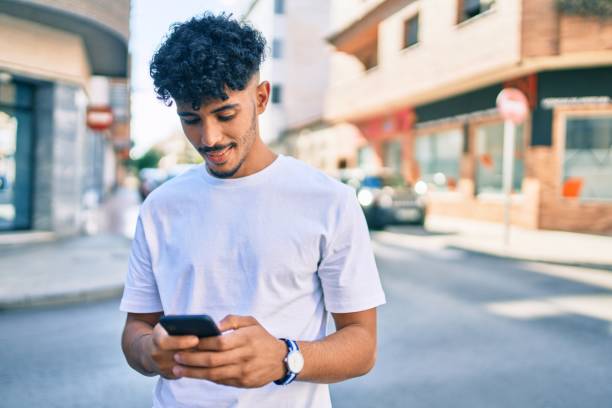 istock Young arab man smiling happy using smartphone walking at city. 1273871803