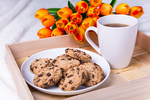 close up of wooden tray with chocolate chip cookies and cup of tea