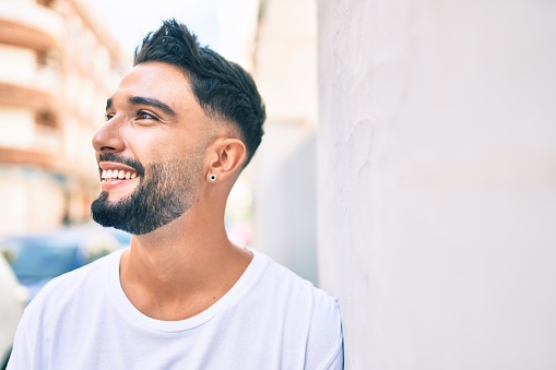 Joven árabe sonriendo feliz apoyado en la pared de la ciudad. photo